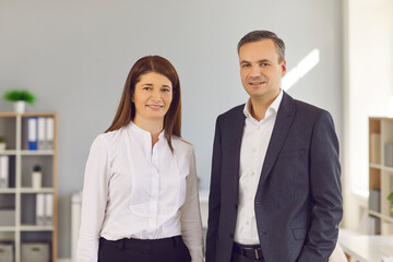 Portrait of office workers woman and man standing in bright office of modern business center and looking at camera. Colleagues are waiting for the beginning of an important meeting with the investor.