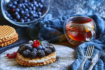homemade waffles with blueberries and blackberries, powdered sugar on a stone plate with fruit. Shallow depth of field.