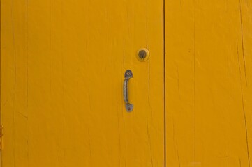 A yellow wooden door background with a rusted iron handle (Pesaro, Italy, Europe)