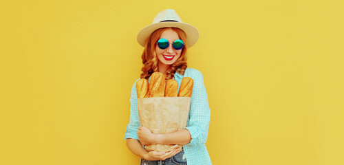 Portrait of happy smiling young woman holding grocery shopping paper bag with long white bread baguette on a yellow background
