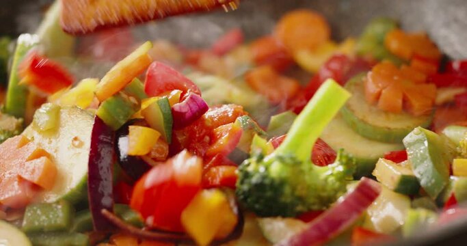 Cooker mixing various colorful vegetables in a frying pan close up shot. Chef cooking healthy vegetarian meal, 4k footage