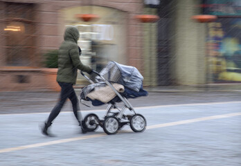 Mother walking with the child in the stroller in snowy winter day. Intentional motion blur