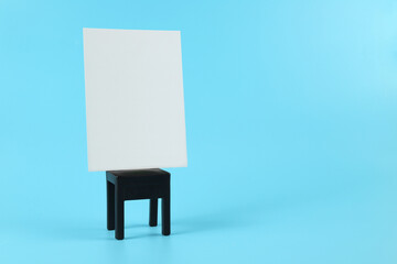 White paper card mockup on a black mini chair against a blue background, copy space.