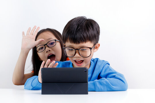 Cute little Asian sibling using tablet doing a video call with family and friend at home during the pandemic lockdown.