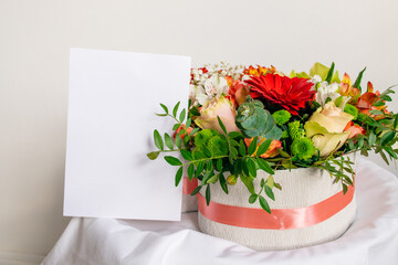 Flowers box with empty white greeting postcard. Mockup. Bouquet of flowers. Valentine's day, Mother's day concept. Branding scene with blank of paper.