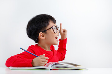 Smart little Asian boy having an idea while doing his homework, looking away sitting at a desk and doing homework. Homeschooling and education concept.