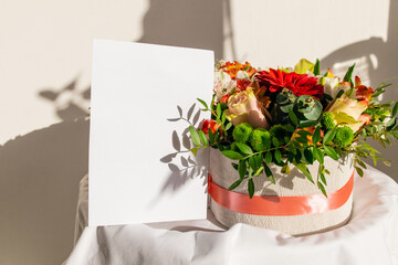 Flowers box with empty white greeting postcard. Mockup. Bouquet of flowers. Valentine's day, Mother's day concept. Branding scene with blank of paper.