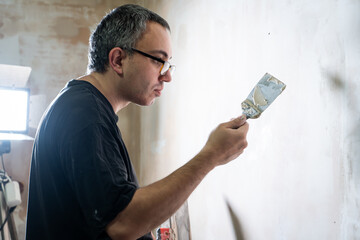 Manual worker with wall plastering tools renovating house. Plasterer renovating indoor walls and...