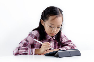 Portrait of little Asian girl using a tablet, sitting at the desk and doing homework. E-learning and education concept.  Isolated on white background