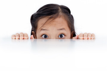 Portrait of an Asian girl peeking through the surface of table isolated on white background.