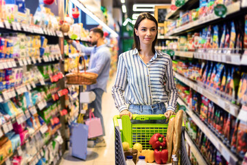 Young casual woman shopping in supermarket with trolley cart