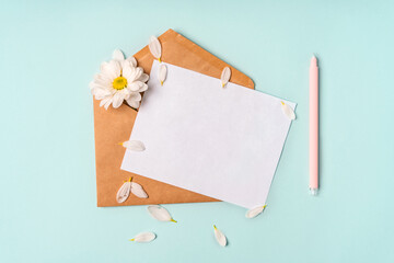 Floral romantic composition. White chamomile flowers and an envelope on a pastel blue background with petals. Valentine's Day, Easter, Birthday, Happy Women's Day, Mother's Day. Top view, copy space