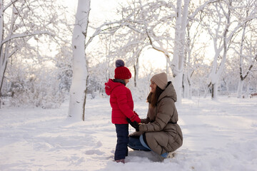 Fototapeta na wymiar Happy mom and daughter 6 years old in a winter snow-covered park hold hands. Family and childhood concept. Holidays and children's parties.