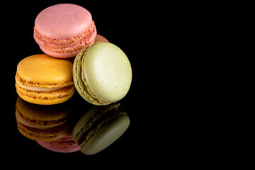French dessert for coffee. Multicolored macarons on black background