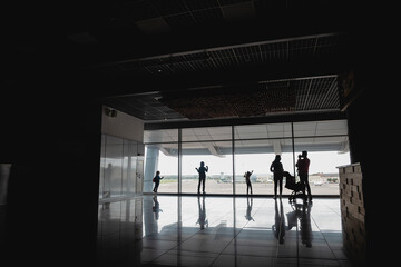 Fototapeta premium Silhouettes of people (family with children) in front of the airport window
