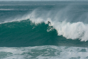 Surfer Carving and performing tricks on huge blue waves in Newquay, Cornwall - Southwest England