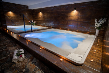 Private whirlpool in a wellness center. Indoor jacuzzi with bubbles. Candles around a whirlpool with blue water. 
