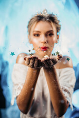 Cute beautiful girl blowing gold stars, stardust from her hands.