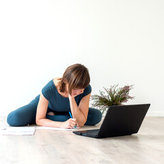 Woman sitting on the floor and writing on a piece of paper next to a laptop