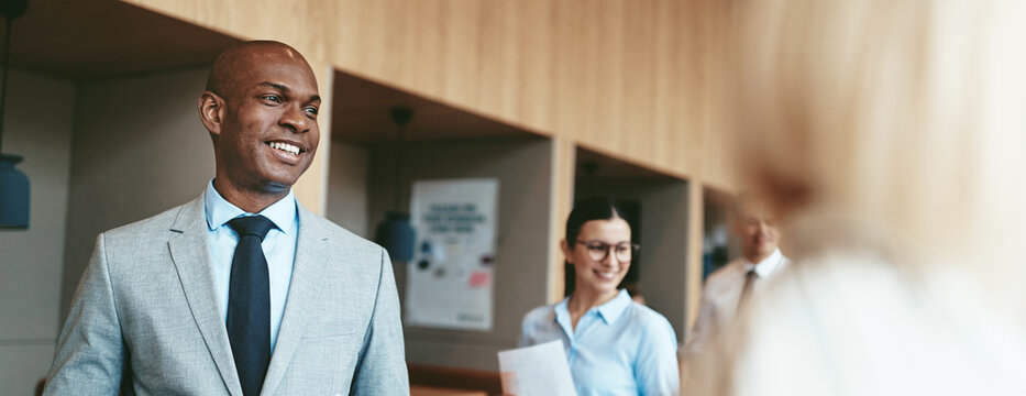 Smiling African American businessman walking with colleagues in an office - Powered by Adobe