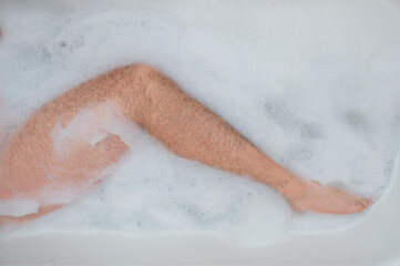 Funny picture of a man taking a relaxing bath. Close-up of male feet in a bubble bath. Top view