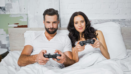 KYIV, UKRAINE - JANUARY 26, 2021: concentrated couple gaming with joysticks in bedroom