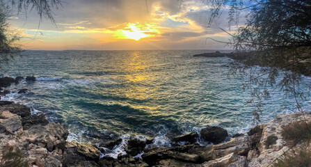 Romantic sunset at sea with waves breaking on the rocks