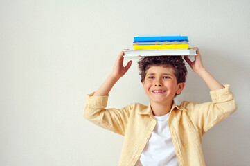 Cute little boy holding many books on his head and smiling. Education background.
