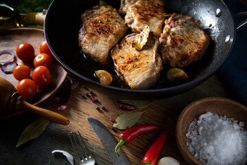 Fried meat in a cast iron pan and vegetables on a rustic table