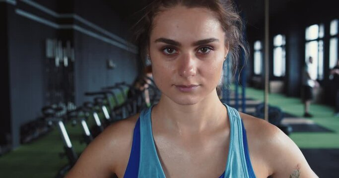 Zoom in portrait of young serious attractive athlete woman looking at camera after workout at modern fitness gym club.