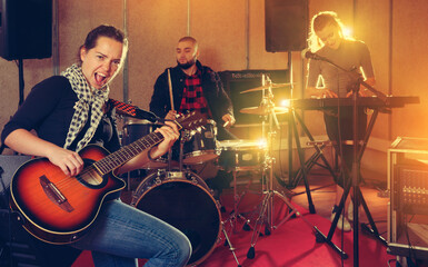 Naklejka premium Rehearsal of music band. Young woman guitar player and singer practicing with band members in recording studio