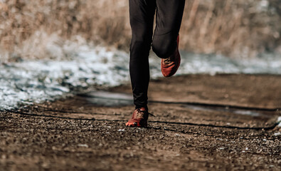 Natural runner outdoors on snowy day on wooden path. Male jogger close up of sport shoes in motion. 
