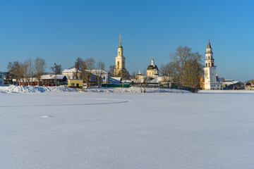Naklejka premium Winter in the ancient city of Nevyansk (Russia). The view from the frozen city pond to the historic center with its famous leaning tower and majestic temple. Pure white snow and pale blue sky 