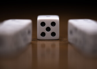 Front view of dice showing a five with two rows of dice leading to it on wood table with reflection