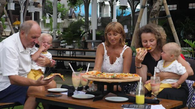 Happy multi-generation family of grandparents, twins and young mom having lunch. Pizza party