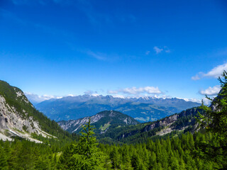 Fototapeta premium A beautiful panorama of Dolomites in Lienz, Austria. Mountain range is spreading endlessly. Few clouds above the peaks. Green trees and bushes overgrowing the slopes.