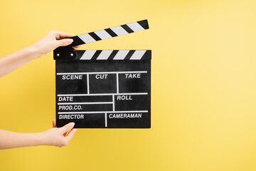 Naklejka premium partial view of camera assistant holding clapperboard isolated on yellow, cinema concept