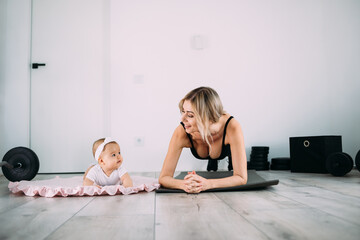 Happy mom and daughter on the floor in the room doing physical exercises on the gymnastic mat at...