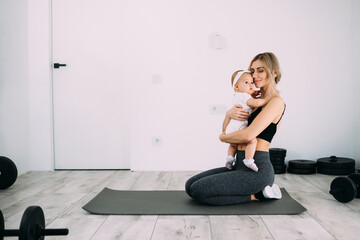 Young beautiful mother with her daughter in her arms sits in the room on the floor after yoga...
