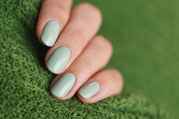 Female neat hand with short natural nails painted with mint nail polish holding knitted green fabrics. Natural, cozy, elegant, modern look.