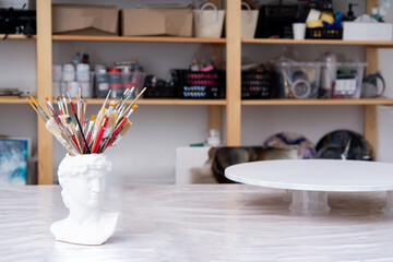 Working workshop of the artist. Plaster vase, stand, brushes, paints, round canvas for painting, shelves. Artist concept.