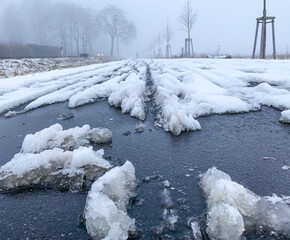 Rutschiger Schneematsch liegt auf einem asphaltierten Fahrradweg. Es ist kalt und nebelig.