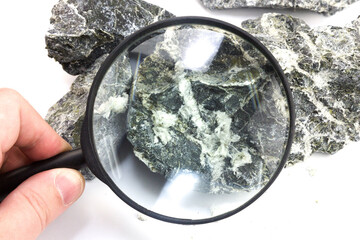 Hand with magnifying glass examines asbestos fibers stone.