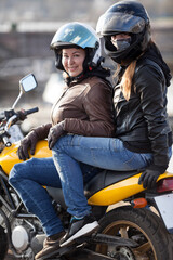 Fototapeta na wymiar Girlfriend a passenger sitting behind female motorcyclist on a motorbike, cheerful females riding on the urban streets