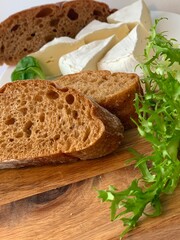 delicious fragrant fresh bread sliced ​​into pieces on a wooden board with herbs and camembert cheese