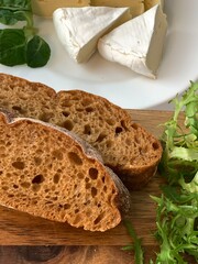 delicious fragrant fresh bread sliced ​​into pieces on a wooden board with herbs and camembert cheese