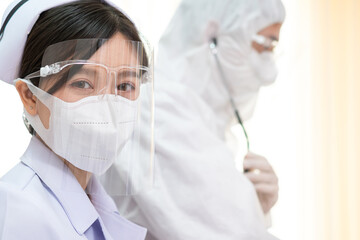 Fototapeta premium Portrait of Thai female nurse wearing protective mask and face shield in hospital. Young Asian medical staff in white uniform. Healthcare concept. copy space
