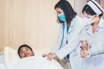 Asian female doctor wearing mask and face shield with nurse using stethoscope checking health of patient sleeping in bed at hospital ward