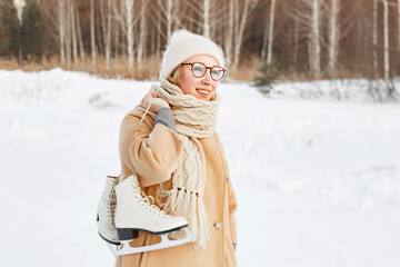 Fototapeta premium young woman in Park near the ice skating rink. girl in beige coat and hat is going to skate, winter leisure and relaxation