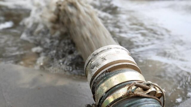 Close-up big pipe of power pump machine pouring mud sludge waste water with sand and silt on ground. Sand-wash and coast-depeening. Septic sewage maintenance service. spring flood deluge aftermath